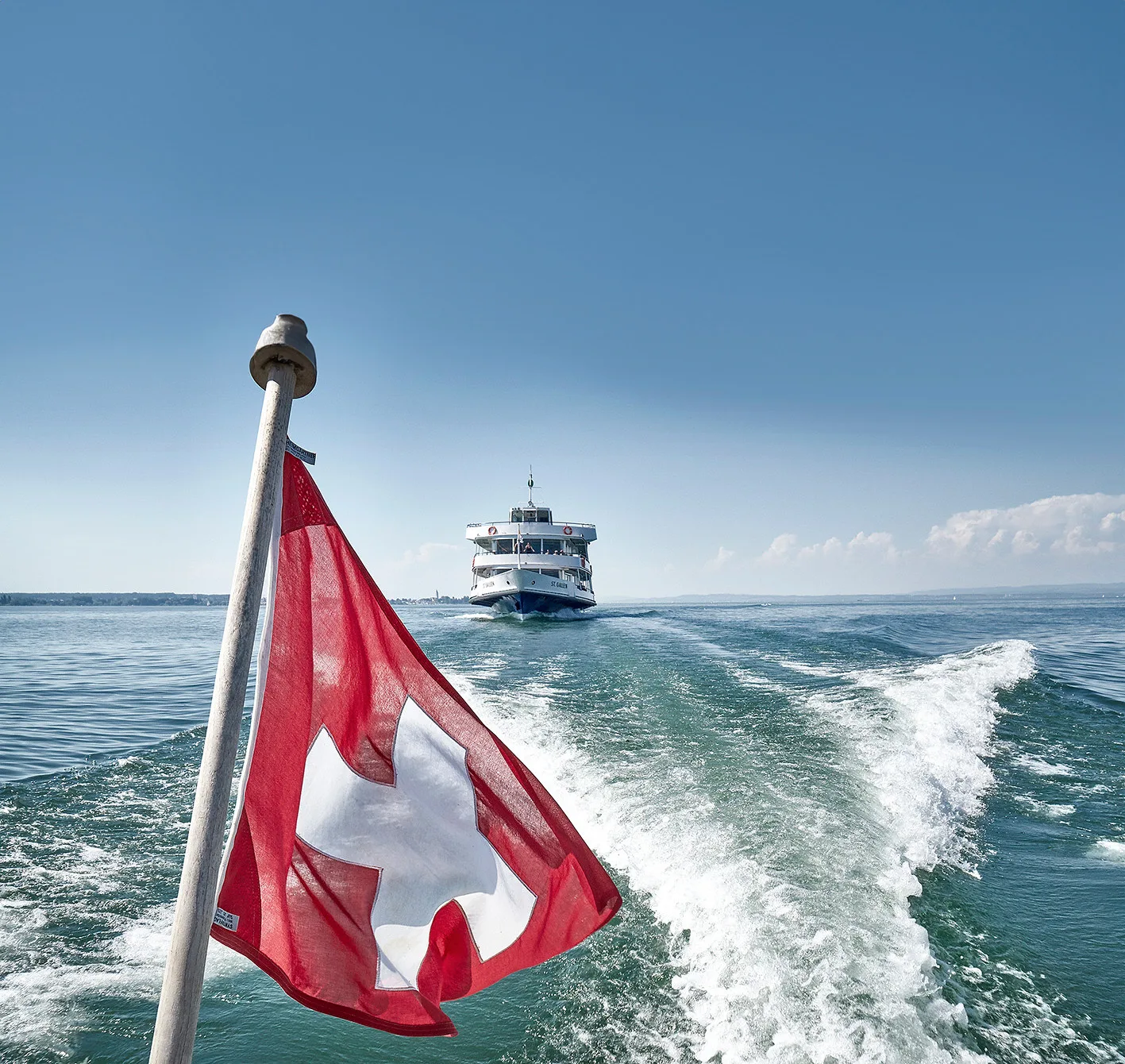 Swiss flag at the stern with a vessel in the wake.